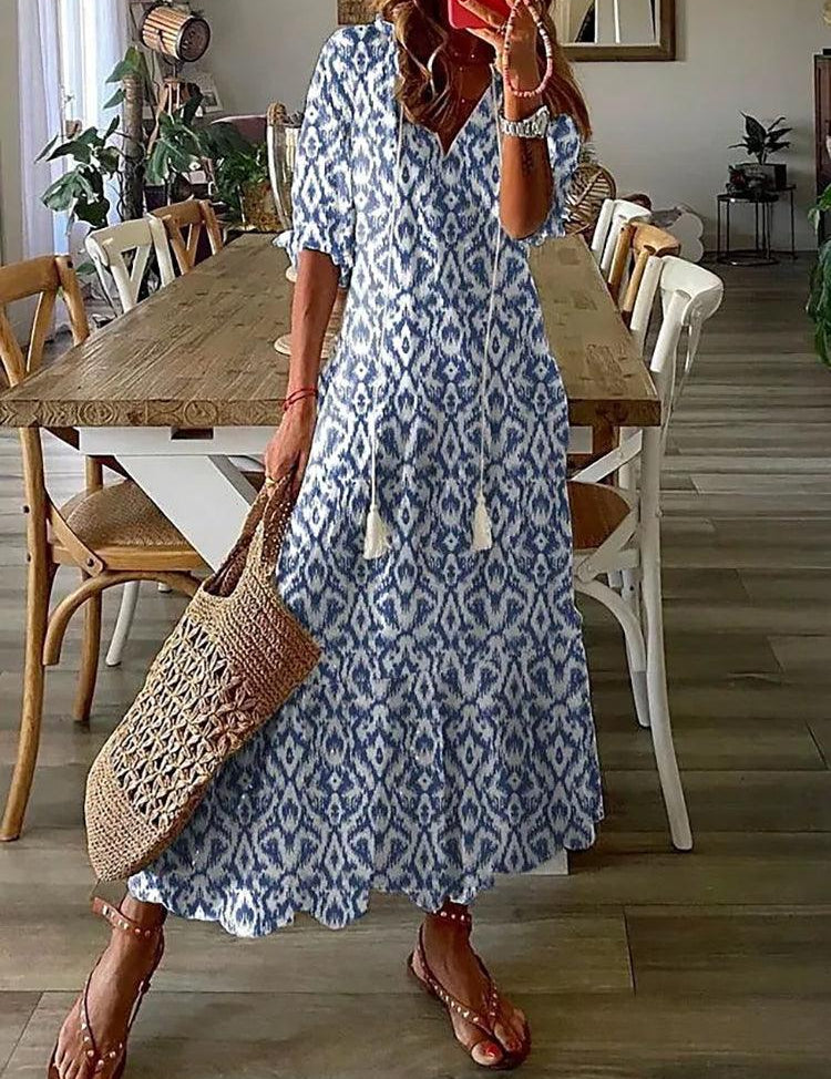 Donna con abito lungo boho blu e bianco, motivo etnico, borsa intrecciata, sandali, in sala da pranzo moderna. Moda estiva casual chic.