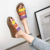 Sandali multicolore da donna con fasce in pelle marrone, gialla, arancione e viola, indossati con jeans chiari. Design estivo e casual.