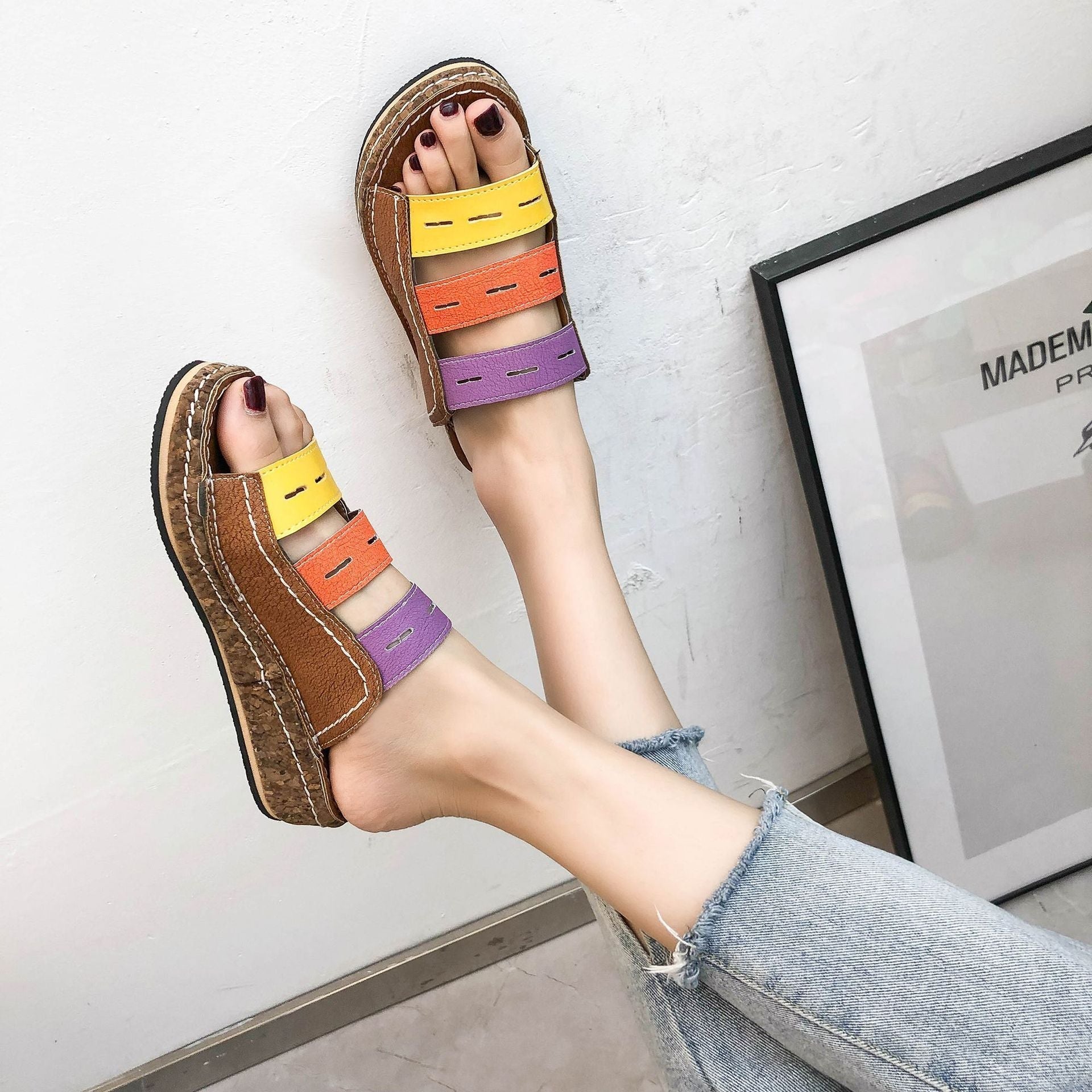 Sandali multicolore da donna con fasce in pelle marrone, gialla, arancione e viola, indossati con jeans chiari. Design estivo e casual.