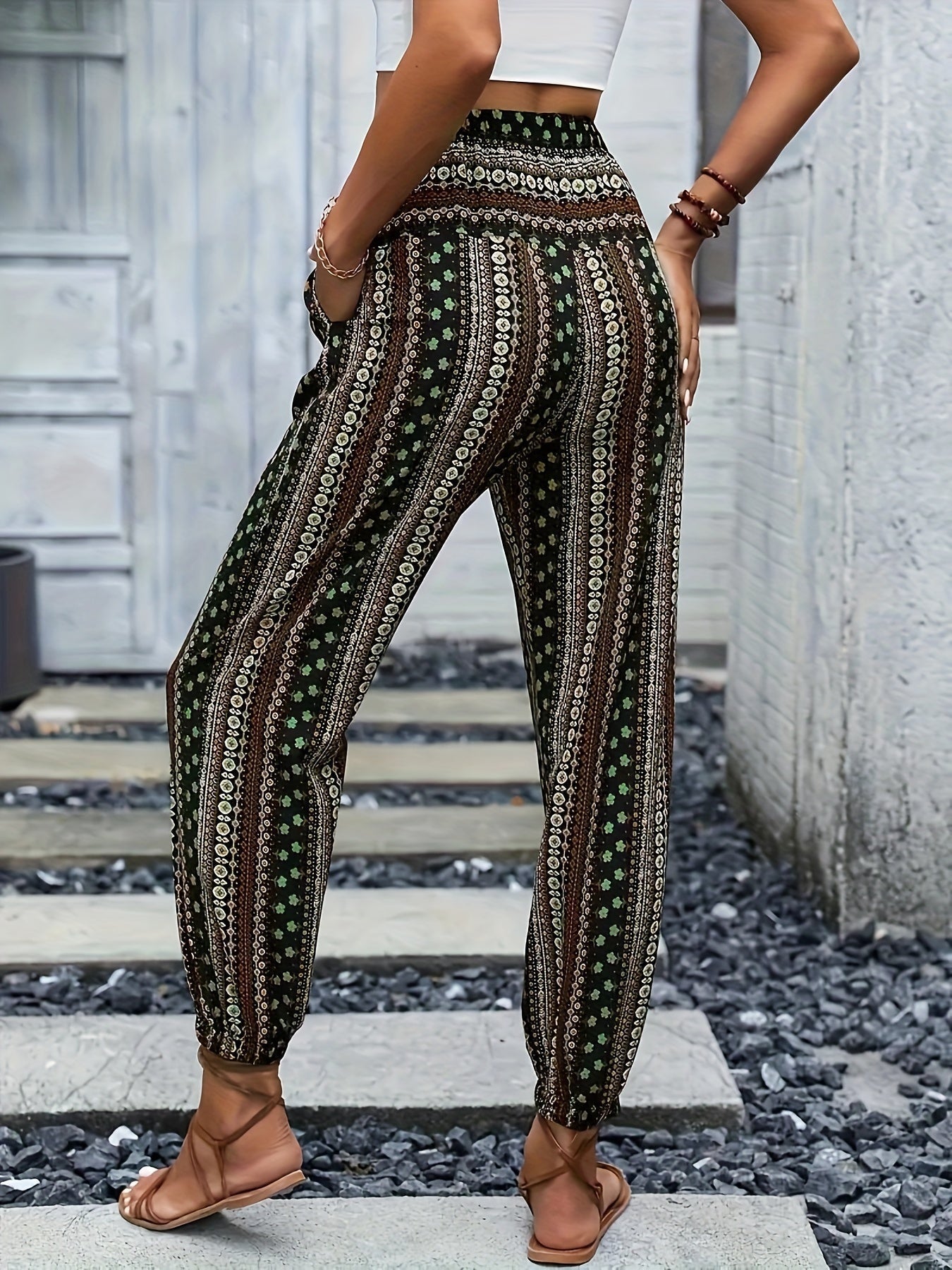 Pantaloni donna a vita alta con stampa etnica, fondo nero e dettagli verdi e bianchi. Moda estiva casual, abbinati a sandali e top bianco.