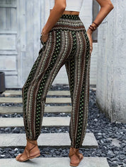 Pantaloni donna a vita alta con stampa etnica, fondo nero e dettagli verdi e bianchi. Moda estiva casual, abbinati a sandali e top bianco.