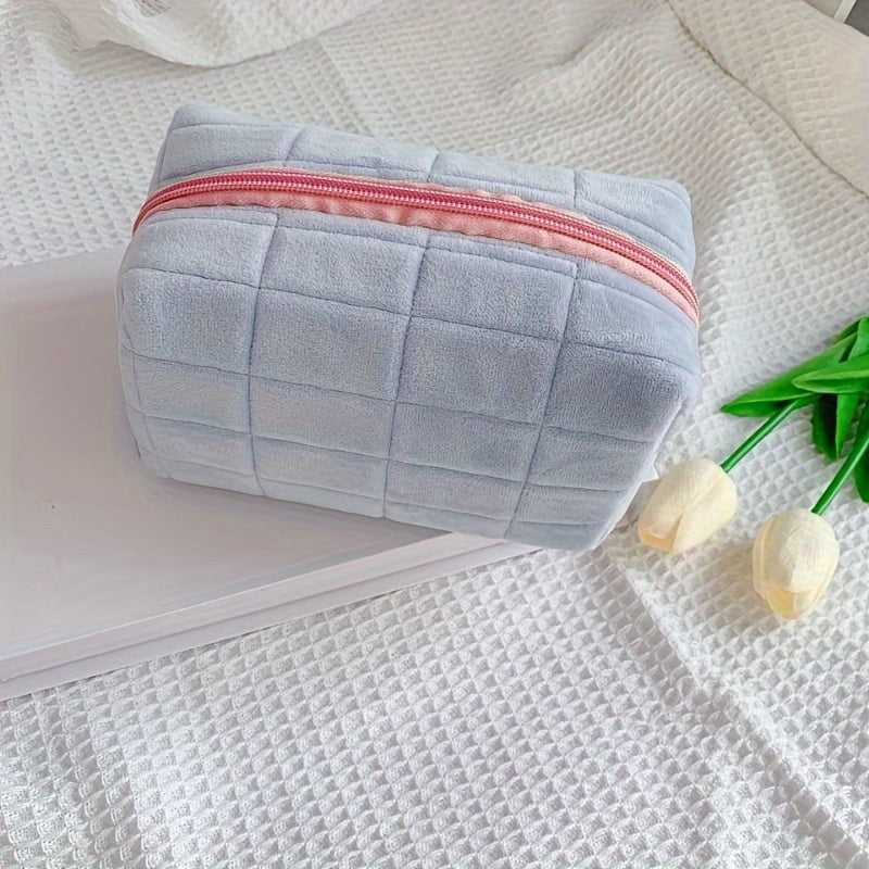 Astuccio cosmetico in tessuto grigio con cerniera rosa su sfondo bianco, accanto a tulipani bianchi. Accessorio da viaggio elegante e pratico.