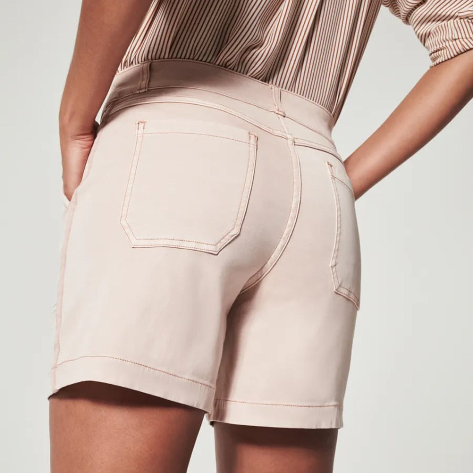 Donna in pantaloncini beige, vista posteriore, con camicia a righe. Moda estiva, abbigliamento casual, tessuto leggero, stile moderno.
