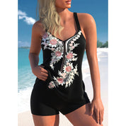 Donna in costume da bagno nero con ricami floreali rosa e bianchi, su spiaggia tropicale. Moda mare, abbigliamento estivo, look elegante.