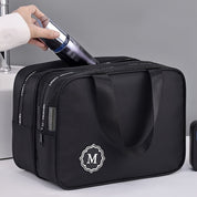 Borsa da viaggio nera con manici, tasche multiple e logo "M". Ideale per organizzare accessori da viaggio. Design elegante e funzionale.
