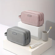 Due beauty case da viaggio in tessuto, uno grigio e uno rosa, su piedistalli bianchi. Include spazzolino e dentifricio. Accessori eleganti e pratici.