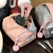 Borsa trucco rosa intrecciata con cerniera aperta, contenente un portacipria nero. Accanto, pennelli trucco e borsa argento. Accessori cosmetici eleganti.