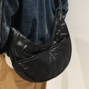 Borsa a tracolla nera in nylon lucido, design moderno e spazioso, indossata su giacca di jeans e pantaloni beige. Accessorio moda unisex.