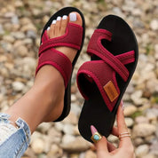 Sandali estivi rossi da donna, con suola nera e design intrecciato, indossati su sfondo di ghiaia. Scarpe comode e alla moda per l'estate.