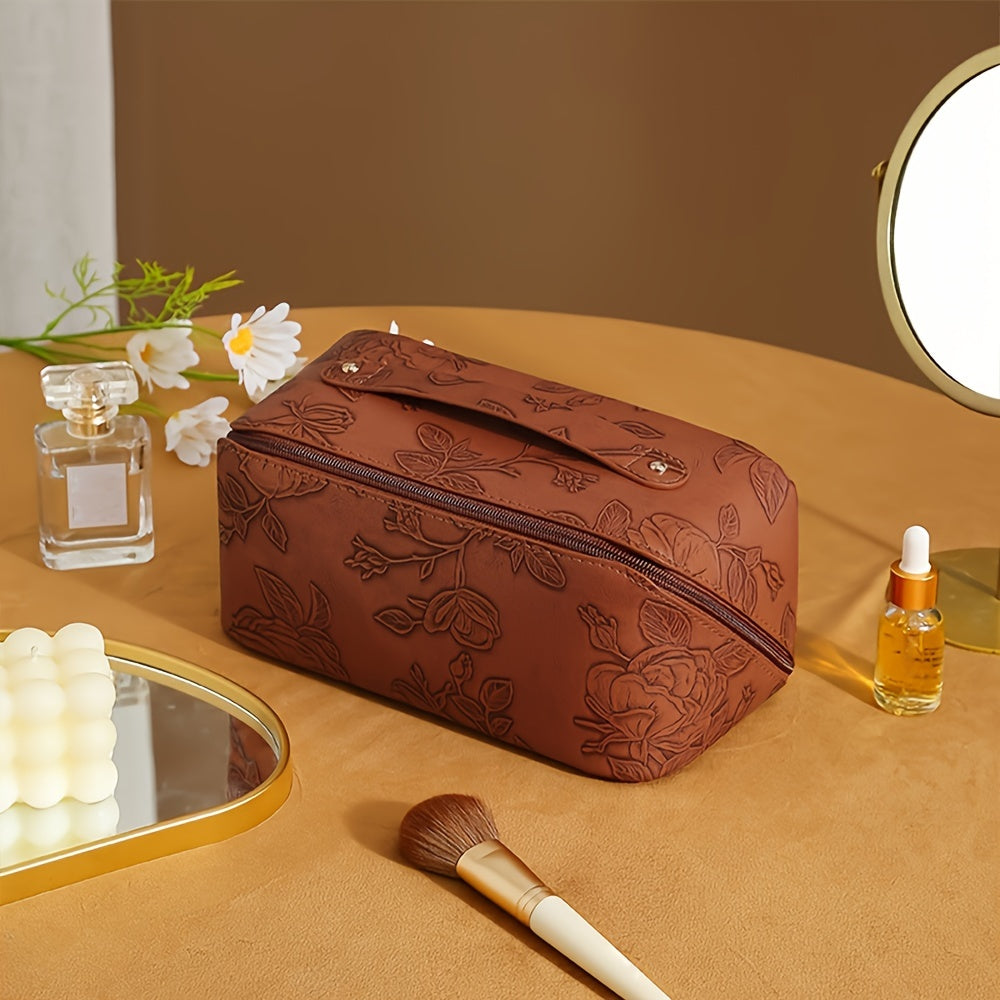 Borsa cosmetica marrone con motivo floreale, su tavolo beige, accanto a specchio, profumo, pennello trucco e olio viso. Accessori bellezza eleganti.