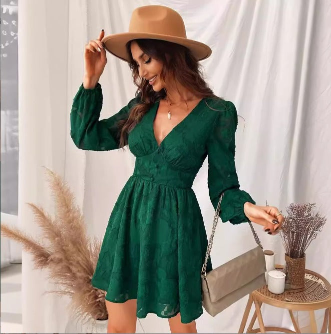 Donna con abito verde elegante, cappello beige, borsa a tracolla, in posa accanto a piante decorative. Moda femminile autunnale chic.