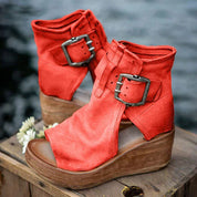 Stivaletti rossi con zeppa in legno, fibbie decorative, design aperto, su tavolo di legno. Scarpe moda donna, stile casual chic.