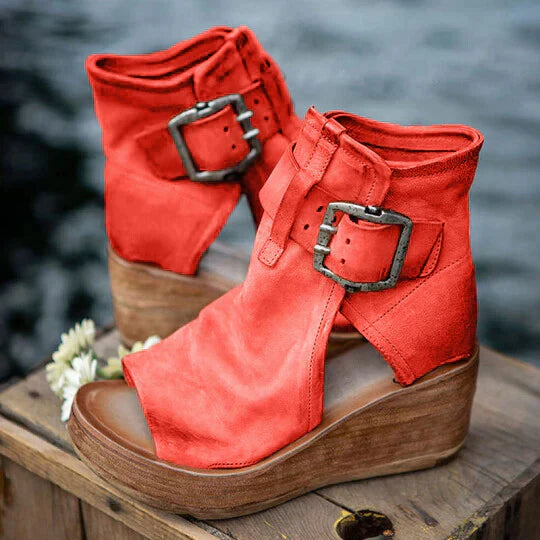 Stivaletti rossi con zeppa in legno, fibbie decorative, design aperto, su tavolo di legno. Scarpe moda donna, stile casual chic.