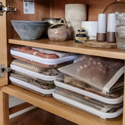 Contenitori sottovuoto per alimenti impilati in un armadio da cucina, accanto a ciotole e spezie. Organizzazione cucina, conservazione cibo.