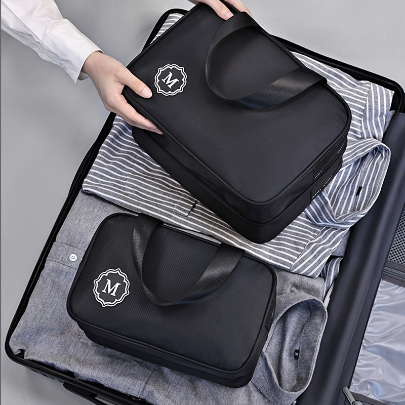 Utente che organizza valigia con borse da viaggio nere, logo "M", su camicie a righe. Accessori viaggio, organizzazione bagagli, valigia ordinata.