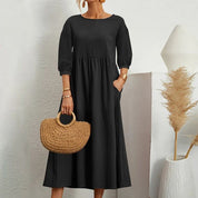 Abito nero lungo donna con maniche a tre quarti, borsa paglia intrecciata, sfondo minimalista bianco, decorazione pampas. Moda elegante casual.