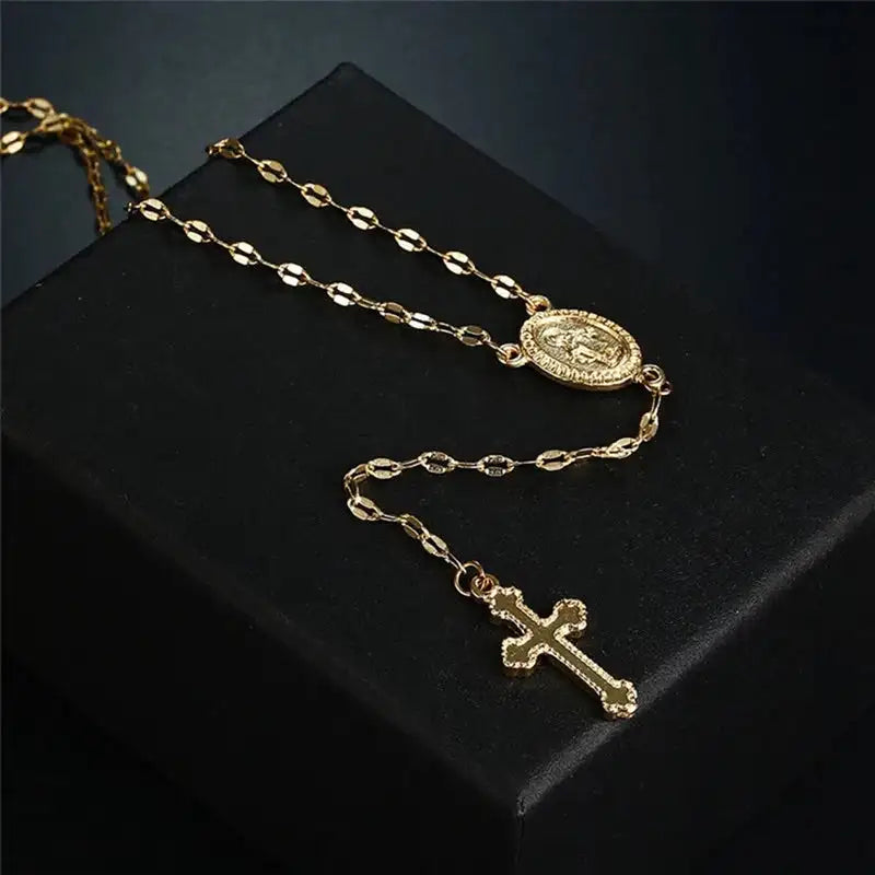 Collana rosario in oro con croce e medaglia su sfondo nero. Gioielli religiosi eleganti, accessori moda, regalo spirituale.
