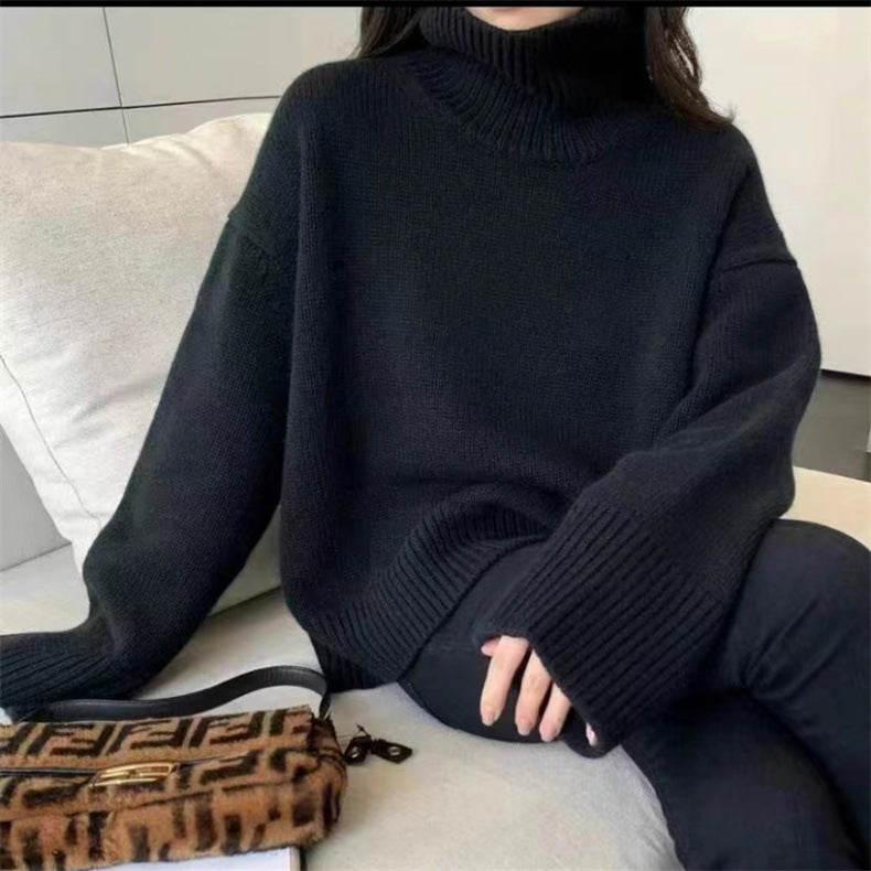 Maglione nero a collo alto in lana, stile oversize, abbinato a borsa Fendi marrone con motivo iconico, su sfondo di divano moderno.