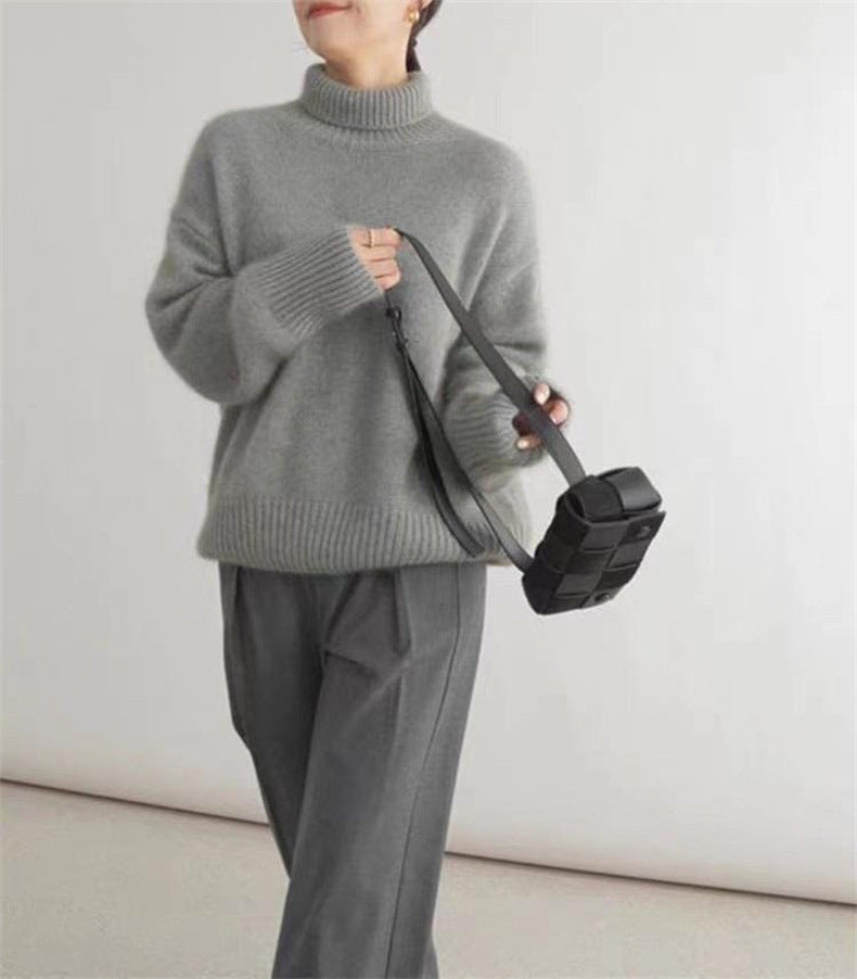 Donna con maglione grigio a collo alto, pantaloni grigi e borsa a tracolla nera. Moda autunnale, abbigliamento casual elegante.