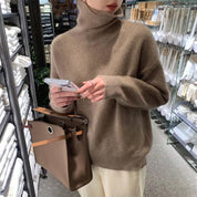Donna con maglione marrone a collo alto, borsa in pelle marrone e smartphone, in negozio di tessuti. Moda autunno inverno, shopping elegante.