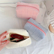 Tre astucci in tessuto morbido a quadri, colori rosa, azzurro e bianco, su sfondo bianco. Ideali per cosmetici e accessori da viaggio.