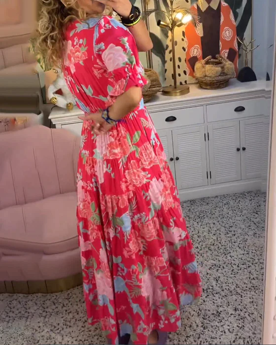 Abito lungo floreale rosso e rosa, donna di spalle in salotto elegante con mobili bianchi e decorazioni artistiche. Moda estiva, stile boho chic.