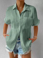 Camicia verde a maniche corte in tessuto plissettato, con colletto classico e taschino, abbinata a shorts di jeans. Moda estiva casual donna.