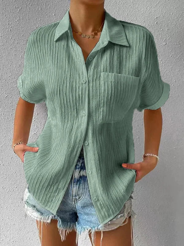 Camicia verde a maniche corte in tessuto plissettato, con colletto classico e taschino, abbinata a shorts di jeans. Moda estiva casual donna.