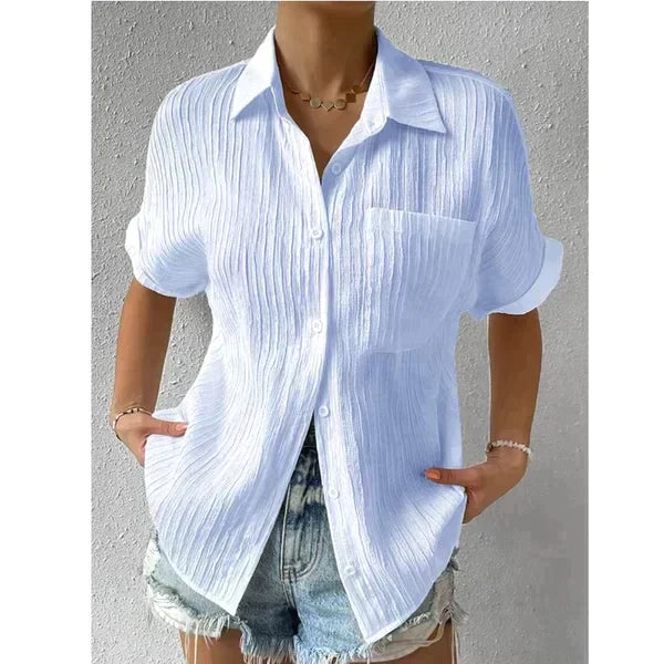 Camicia bianca a righe verticali, maniche corte, indossata con pantaloncini di jeans. Stile casual estivo, moda donna, tessuto leggero.