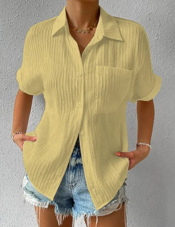 Camicia gialla a maniche corte in tessuto plissettato, abbinata a shorts di jeans. Look estivo casual per donna.