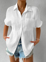 Camicia bianca a maniche corte in tessuto leggero, con colletto classico e taschino, abbinata a shorts di jeans. Look estivo casual donna.