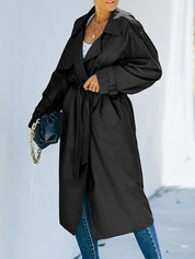 Cappotto trench nero da donna, elegante e lungo, con cintura in vita. Indossato sopra jeans e top bianco. Moda autunnale, stile casual chic.