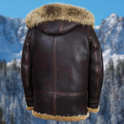 Giacca in pelle marrone con cappuccio e bordo in pelliccia, sfondo montagna innevata. Abbigliamento invernale uomo, stile elegante e caldo.