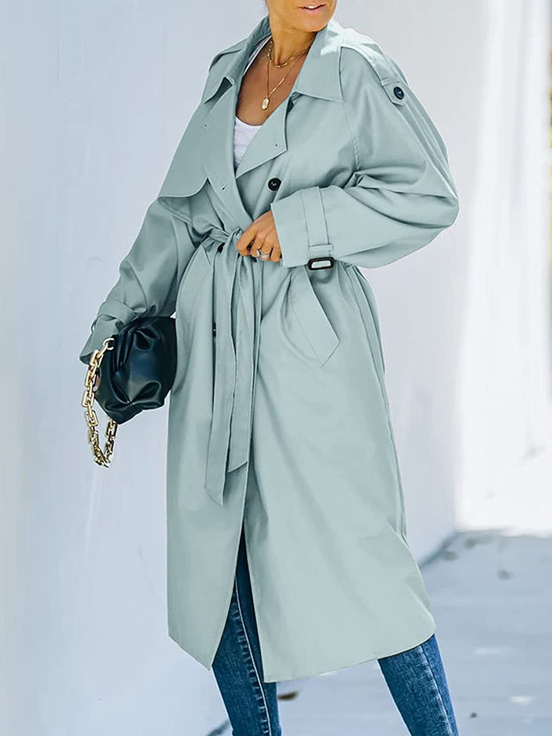 Cappotto trench donna elegante azzurro, cintura in vita, tasche laterali, abbinato a jeans e borsa nera. Moda autunnale chic.