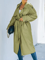 Cappotto trench verde oliva da donna, lungo, con cintura in vita, abbinato a jeans blu e borsa nera. Stile elegante e moderno per l'autunno.