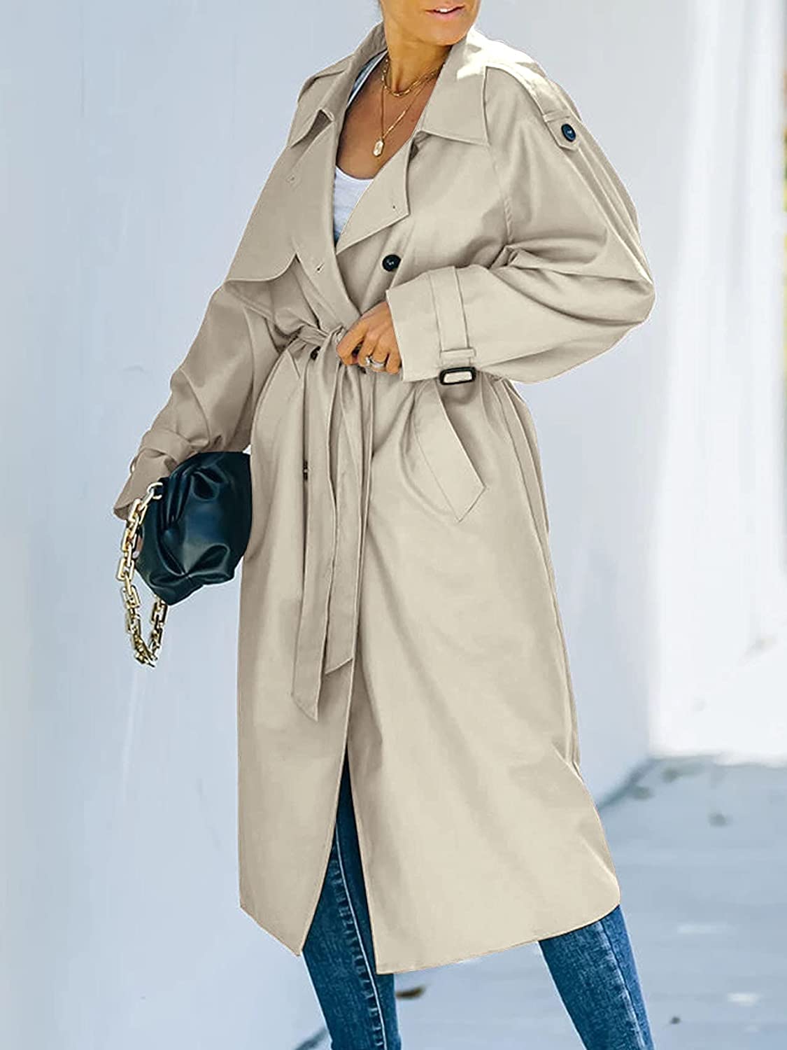 Cappotto trench beige da donna, elegante e lungo, con cintura in vita e bottoni, abbinato a jeans blu. Moda autunnale, stile casual chic.