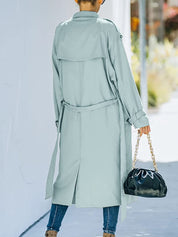 Donna con trench verde chiaro, jeans e borsa nera a catena dorata. Moda autunnale, stile urbano elegante. Sfondo urbano sfocato.