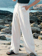 Pantaloni larghi bianchi in lino, donna, su spiaggia rocciosa. Moda estiva, abbigliamento casual, comfort, stile elegante.