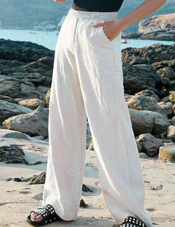 Pantaloni larghi bianchi in lino, donna, su spiaggia rocciosa. Moda estiva, abbigliamento casual, comfort, stile elegante.