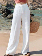 Pantaloni bianchi larghi da donna in lino, indossati su spiaggia estiva. Moda estiva, abbigliamento casual, stile vacanza.