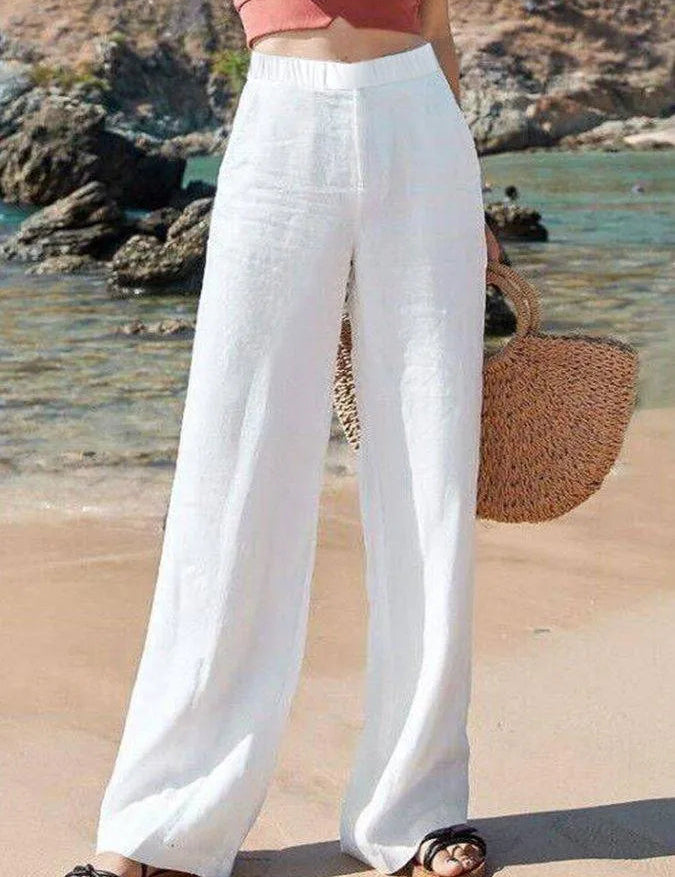 Pantaloni bianchi larghi da donna in lino, indossati su spiaggia estiva. Moda estiva, abbigliamento casual, stile vacanza.
