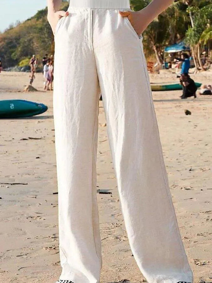 Pantaloni larghi bianchi in lino su spiaggia, moda estiva donna, abbigliamento casual, comfort e stile, tendenza mare 2023.