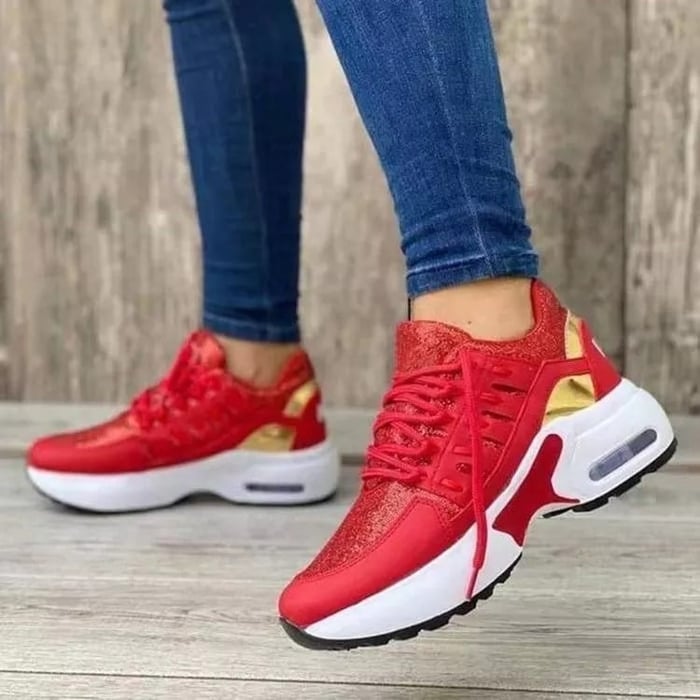 Scarpe da ginnastica rosse e oro da donna, suola bianca, indossate con jeans. Design moderno, comode per sport e tempo libero.