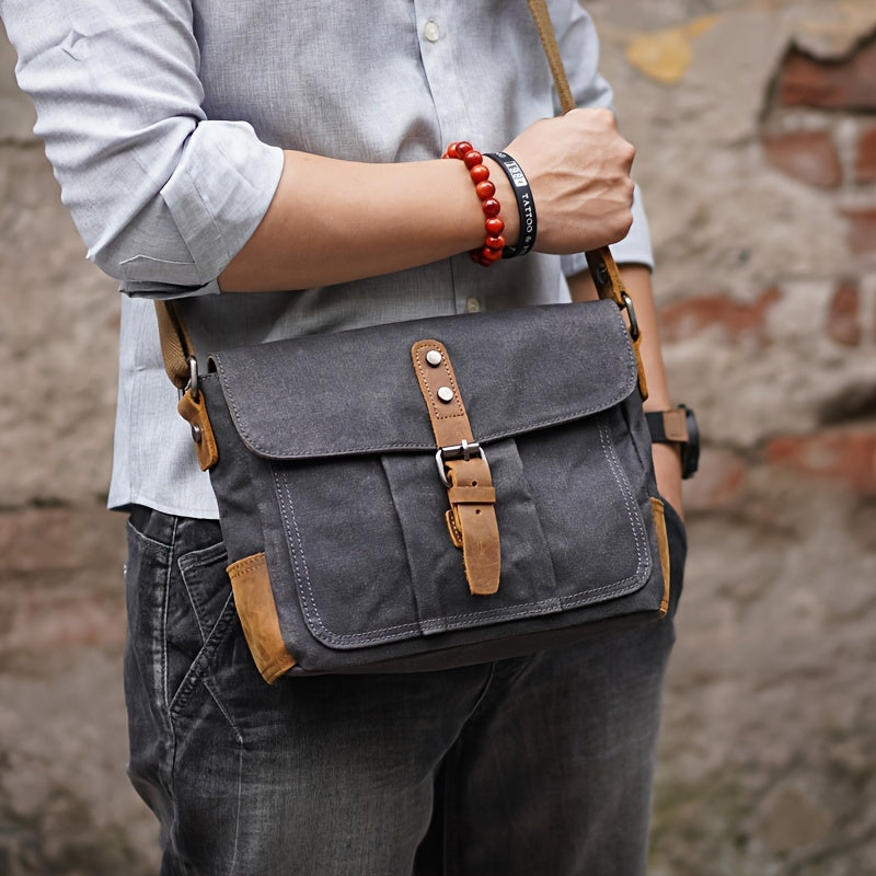 Uomo con borsa a tracolla in tela grigia, dettagli in pelle marrone, indossa camicia azzurra e bracciale rosso. Stile casual urbano.