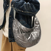 Borsa a tracolla argentata in tessuto lucido, indossata da una persona con giacca di jeans e pantaloni beige. Accessorio moda casual e trendy.