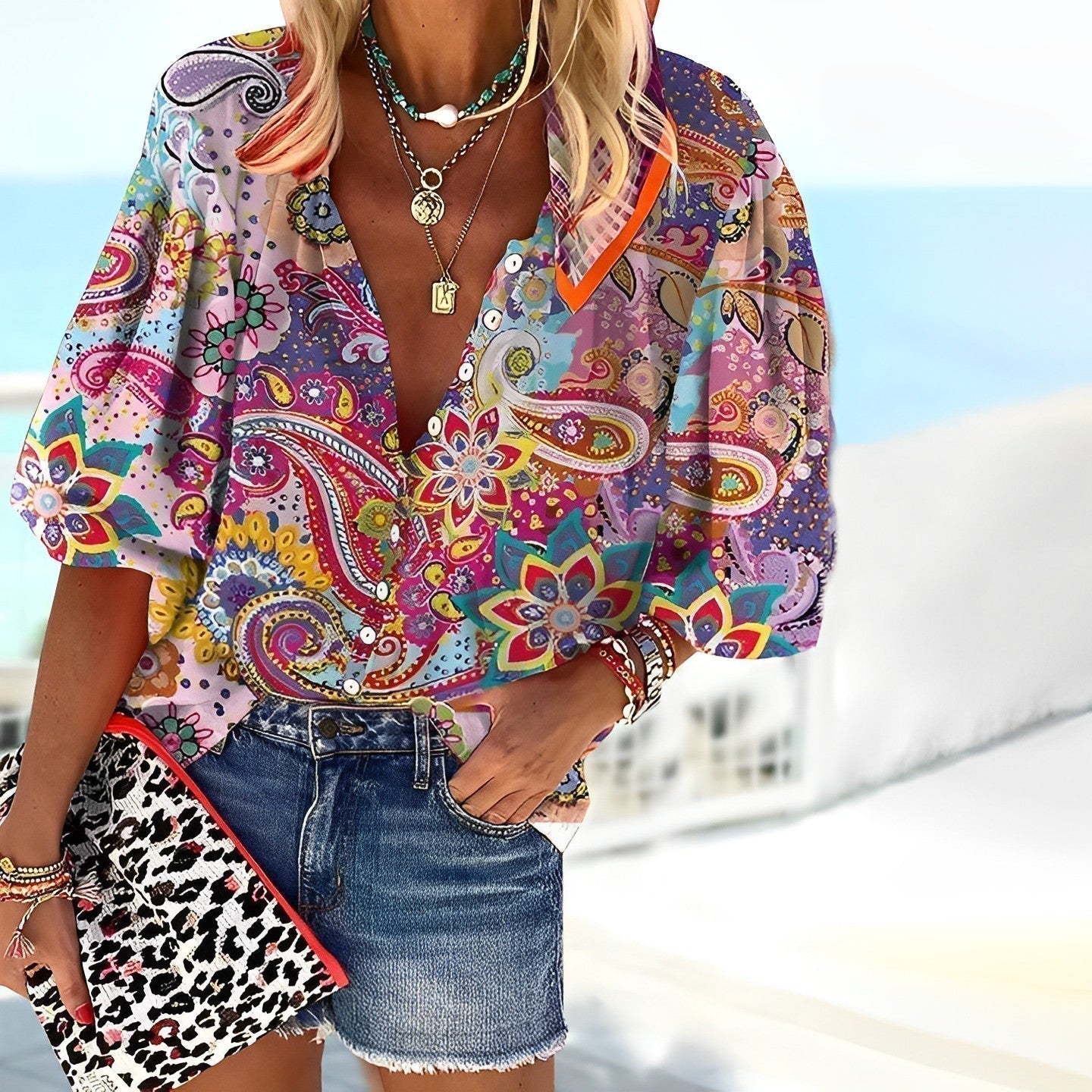Donna con camicia a fantasia paisley colorata, collane e borsa leopardata, indossa shorts di jeans. Look estivo alla moda, accessori trendy.