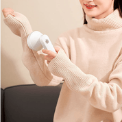 Donna con maglione beige utilizza un dispositivo per rimuovere pelucchi da vestiti. Accessorio per la cura dei tessuti, pratico e portatile.