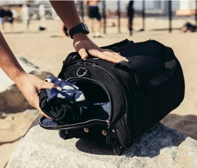 Borsa da palestra nera su spiaggia, con tasca aperta e abbigliamento sportivo. Ideale per fitness, viaggio, resistente e spaziosa.