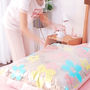 Persona utilizza un aspirapolvere per comprimere un sacco sottovuoto con cuscino floreale. Organizzazione casa, risparmio spazio, sacchi sottovuoto.