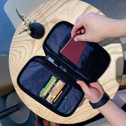 Portafoglio organizer nero aperto su tavolo in legno chiaro, con carte di credito colorate e passaporto. Mano che inserisce documento. Accessorio viaggio.